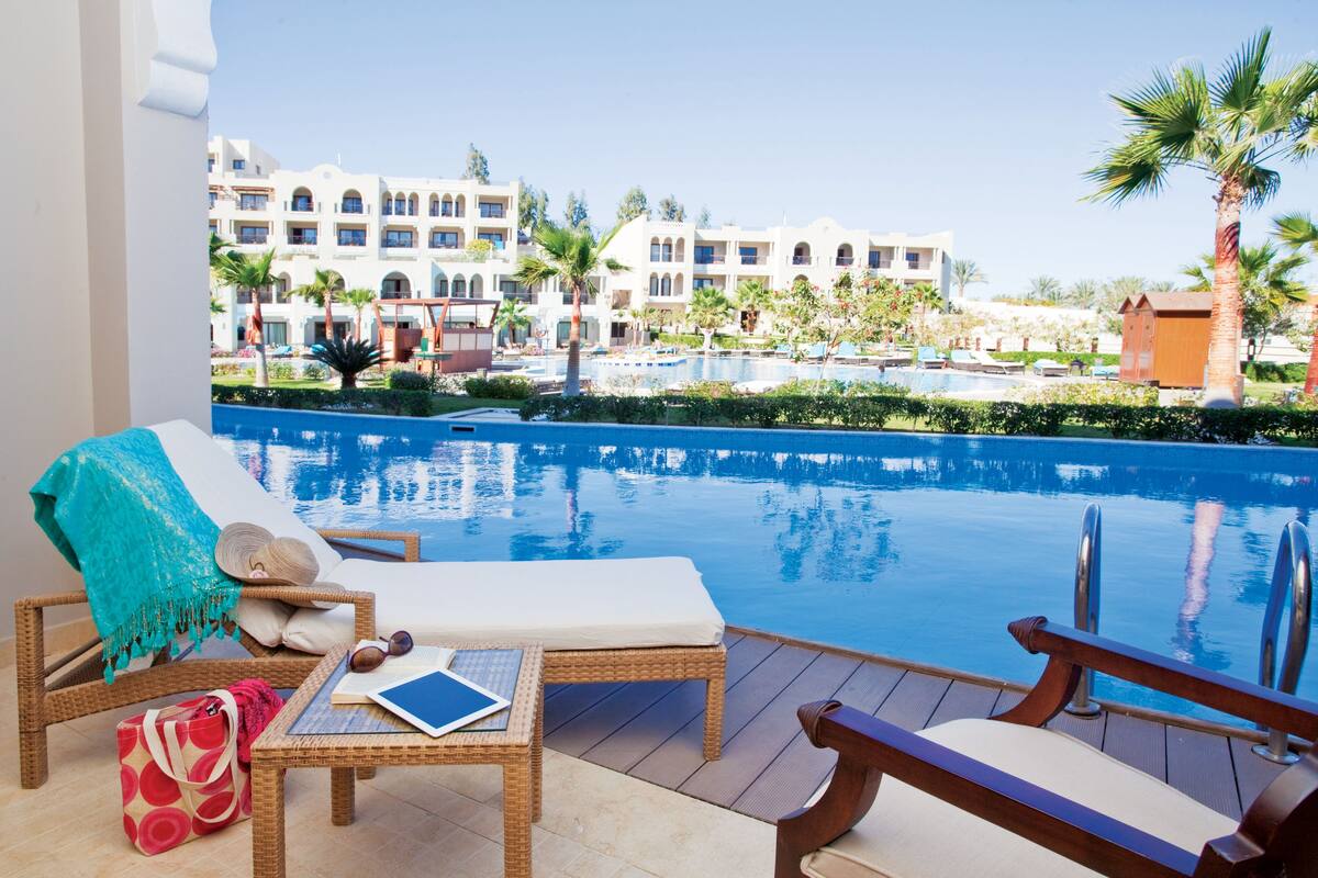 A poolside area with lounge chairs, a table, and a view of a resort building.