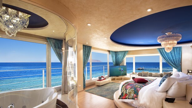 A luxurious bedroom with a large bed, a bathtub, and a view of the ocean. - SUNRISE Arabian Beach Resort (Sharm El Sheikh)