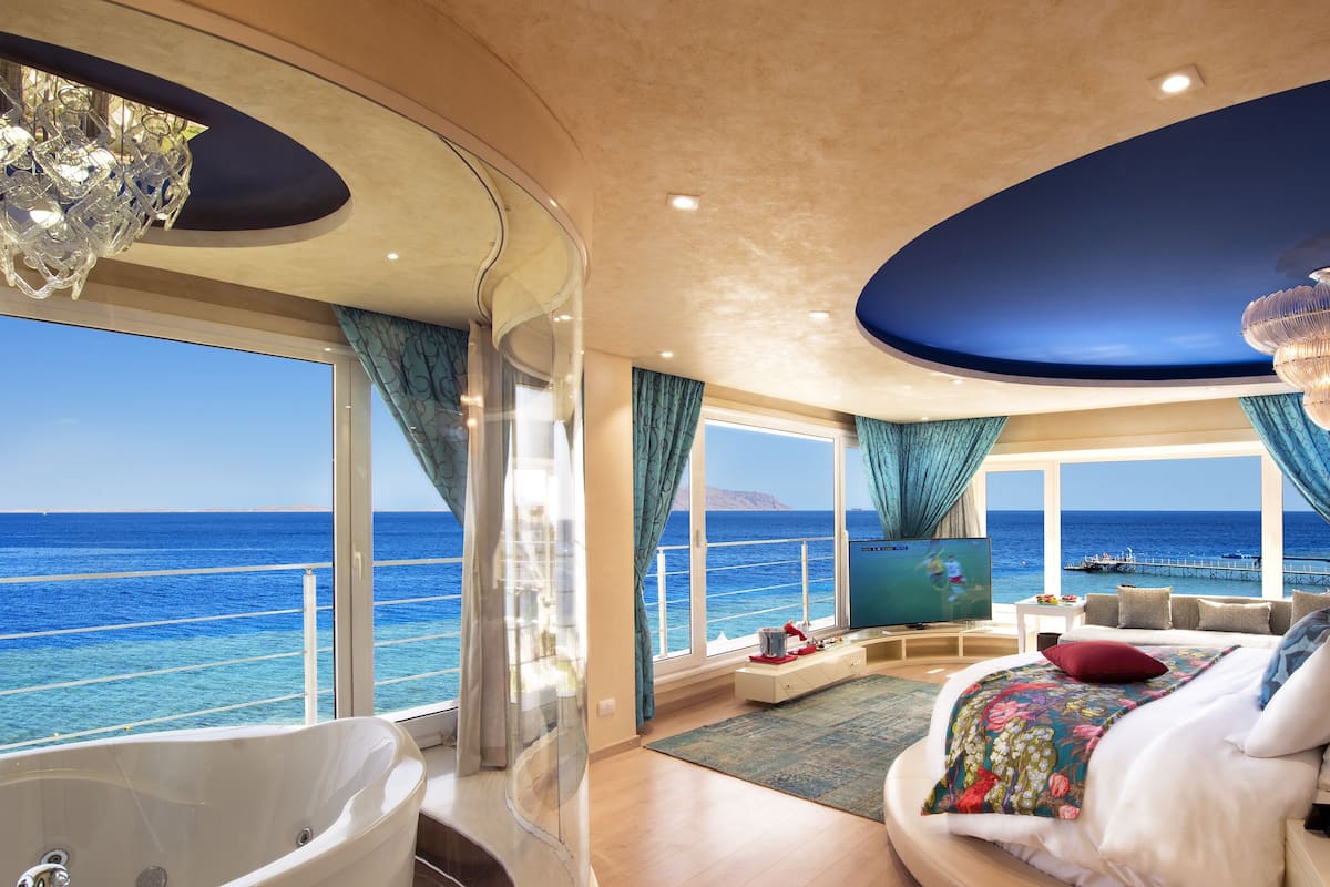 A luxurious bedroom with a large bed, a bathtub, and a view of the ocean.