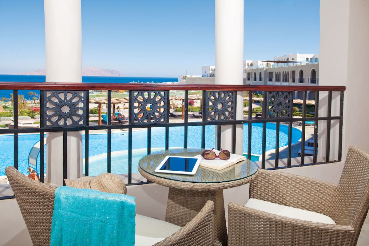 A balcony with wicker furniture, a tablet, and sunglasses, overlooking a pool and a resort area.