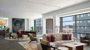 A modern lounge area with sofas, chairs, a coffee table, and large windows offering views of the cityscape.