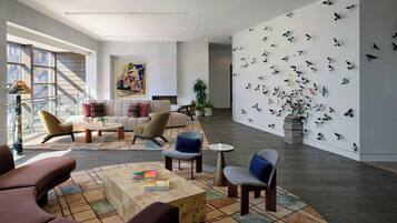 Un hall espacioso con diseño moderno, que cuenta con una zona de estar con sofás y sillones, una gran obra de arte en la pared y una pared decorada con motivos de pájaros.