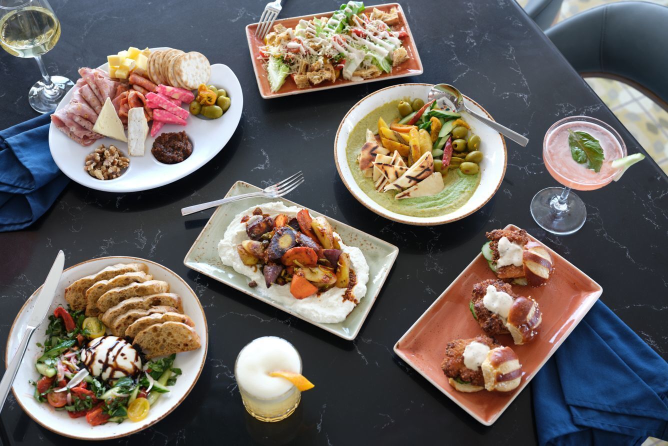 A table with various dishes and drinks, including a charcuterie board, salads, and a martini.
