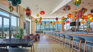 A modern bar area with a long counter, multiple bar stools, and colorful hanging lanterns.