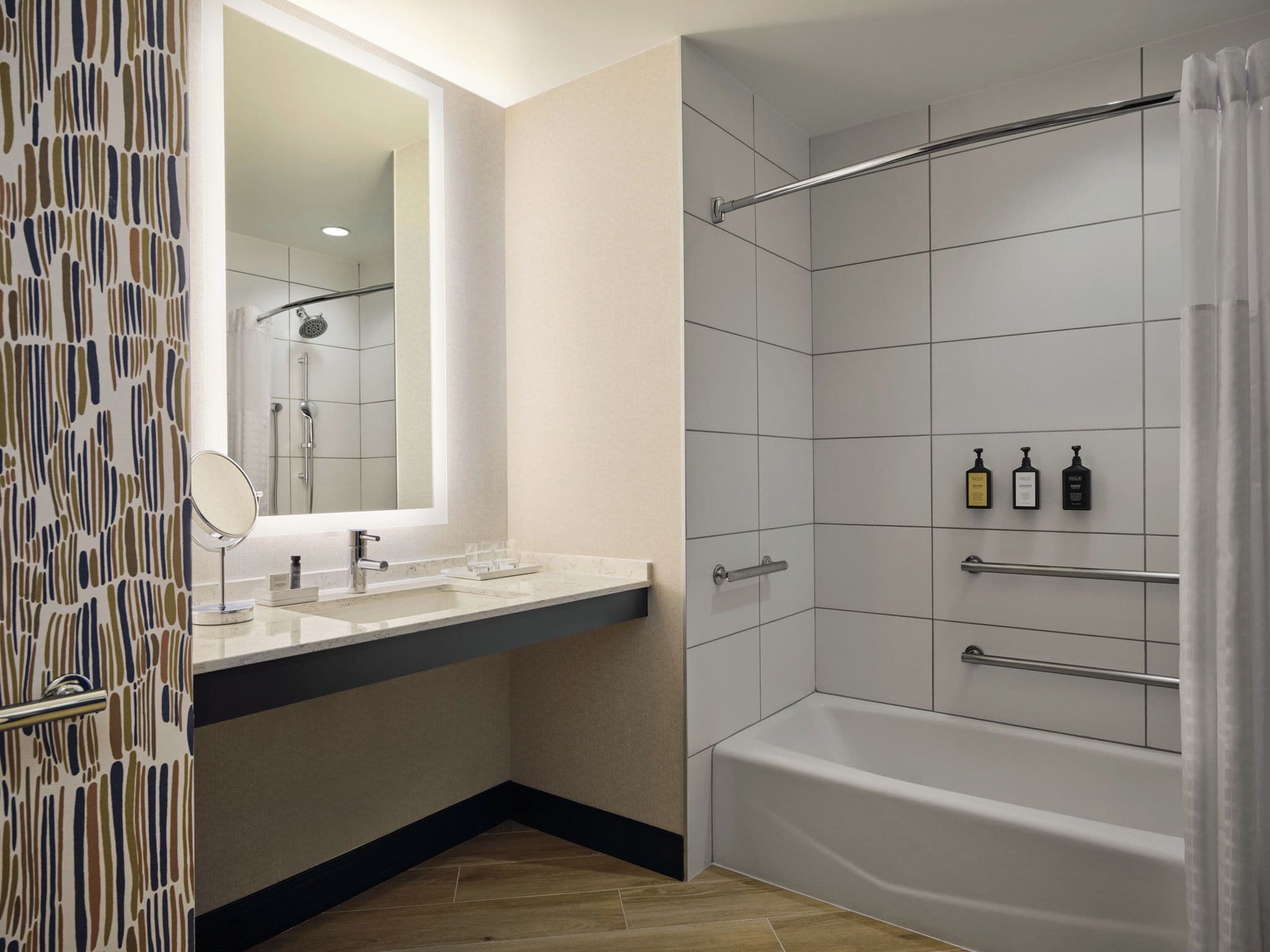 A modern bathroom with a bathtub, a shower, a vanity with a mirror, and toiletries on a shelf.