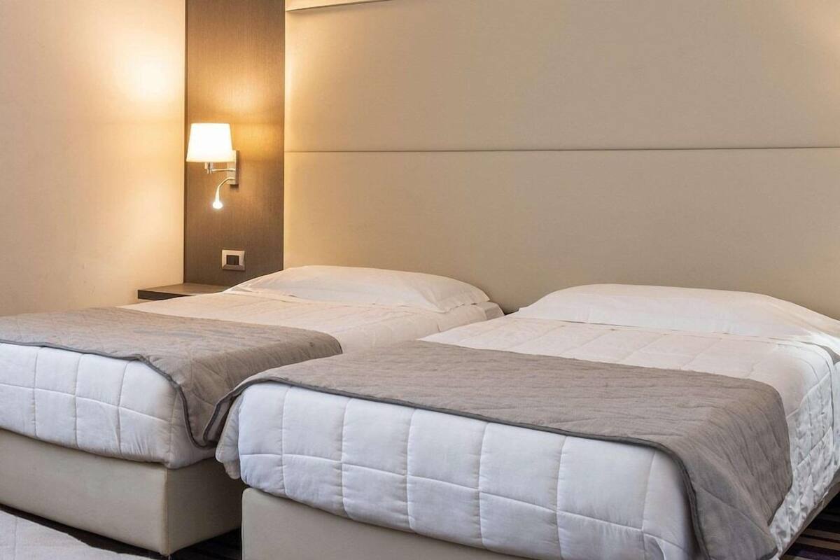 A hotel room with two beds, a wall-mounted light, and a neutral color scheme.