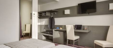 A modern hotel room with a large bed, a desk with a laptop, a television, and a small seating area.