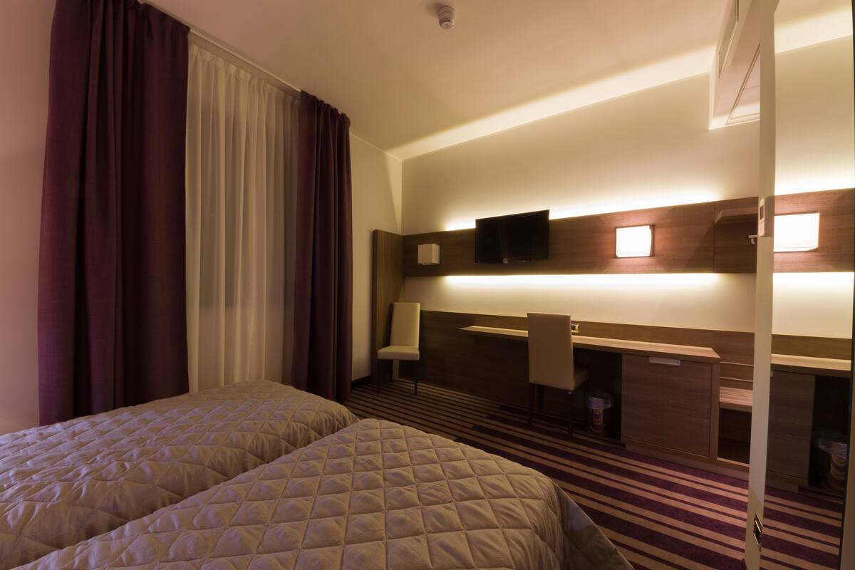 A hotel room with two beds, a desk, a chair, a television, and a minibar.