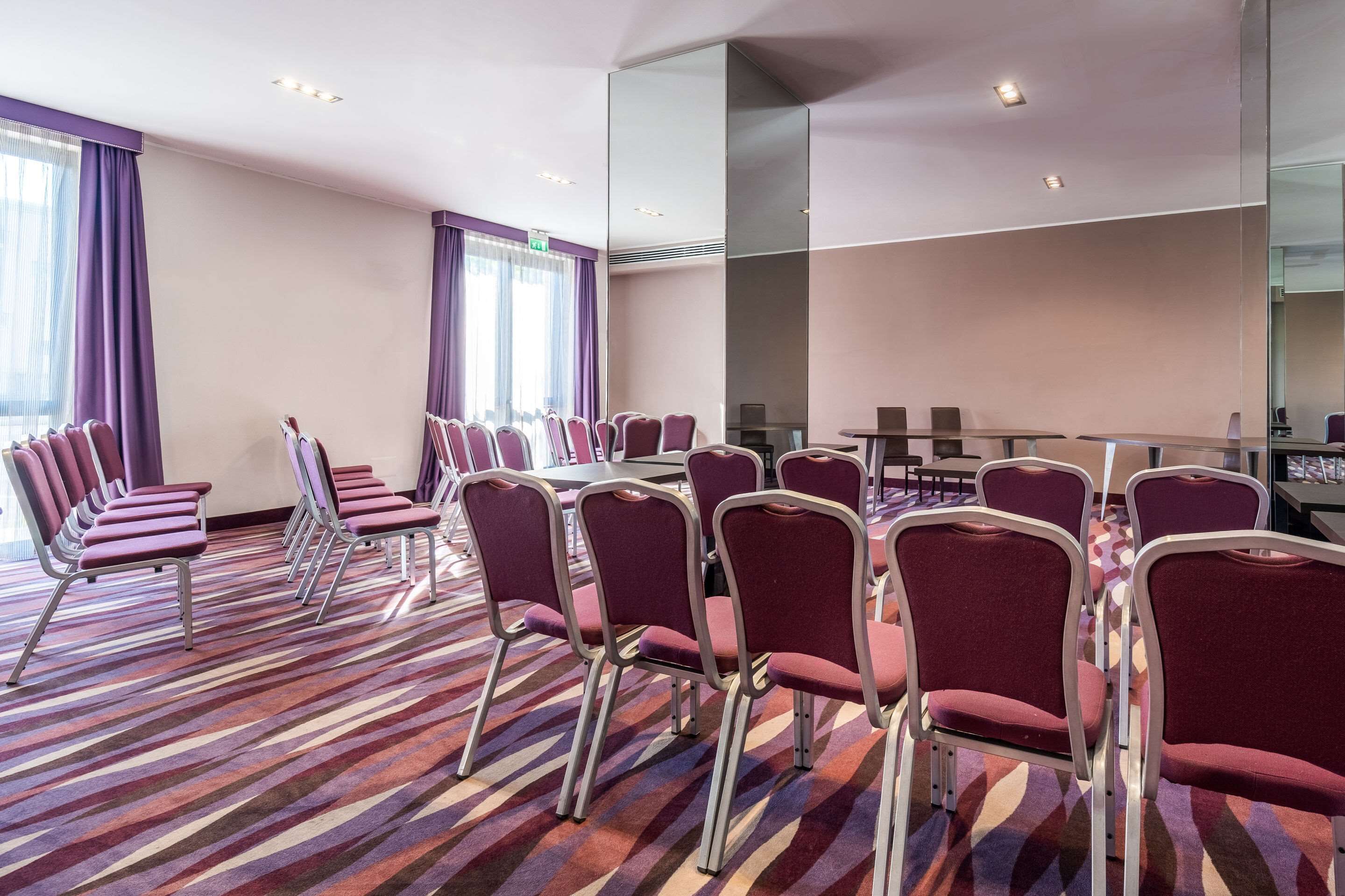 A conference room with rows of chairs, a large mirror, and a patterned carpet.