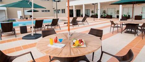 An outdoor patio with a round wooden table, wicker chairs, and umbrellas.