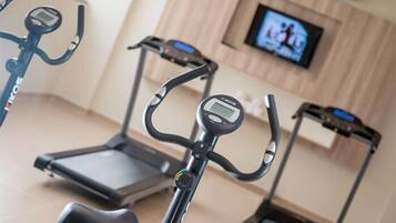 A home gym with treadmills and stationary bikes, a TV mounted on the wall, and a wooden floor.