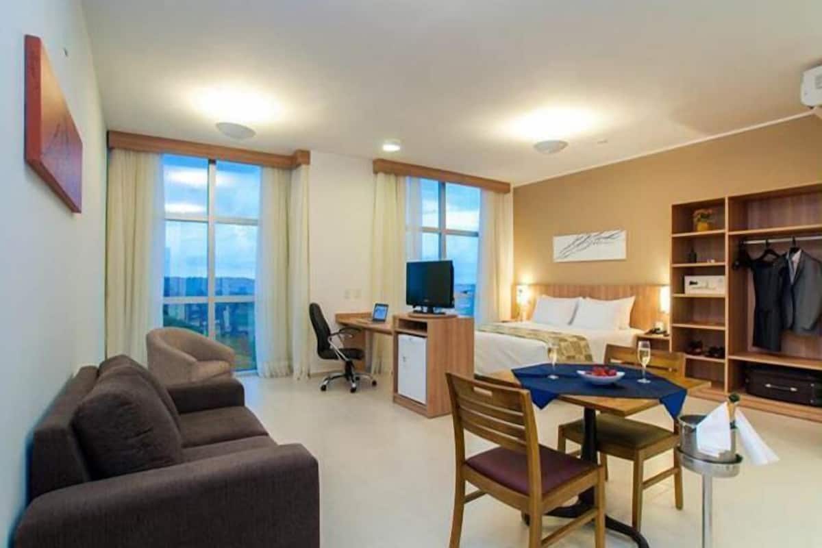 Habitación de hotel con cama, escritorio, silla, televisión y zona de comedor con mesa y sillas.