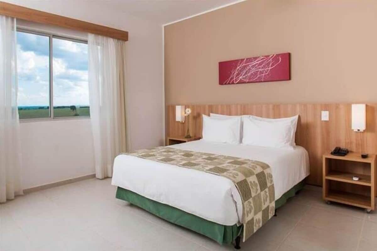 Habitación de hotel con una cama grande, vistas al exterior, cabecera de madera y un cuadro abstracto rojo en la pared.