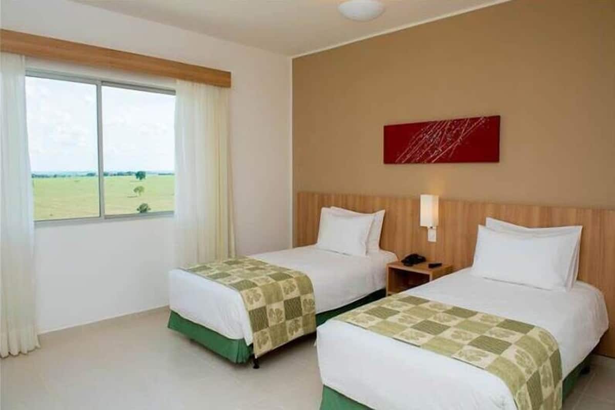 Habitación de hotel con dos camas, un ventanal con vistas a un campo verde y un cuadro abstracto rojo en la pared.