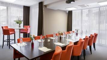 A conference room with a long table, orange chairs, water bottles, and a projector.