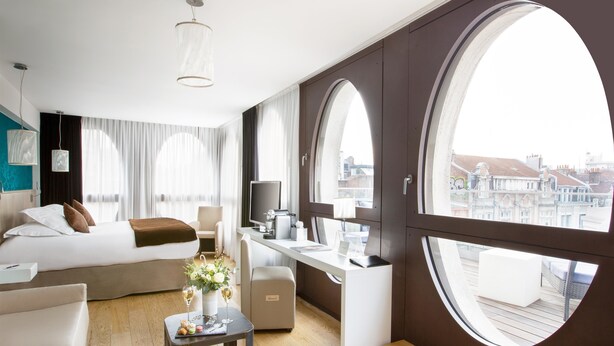 A modern hotel room with a large bed, a desk, and a view of the city through large windows. - Best Western Premier Why Hotel (Lille)