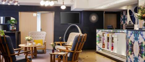 A modern hotel lobby with wooden furniture, a television, and a decorative wall.