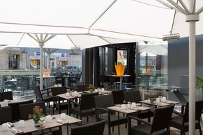 An outdoor cafe with tables and chairs, a glass wall, and a view of the street. - Best Western Premier Why Hotel (Lille)