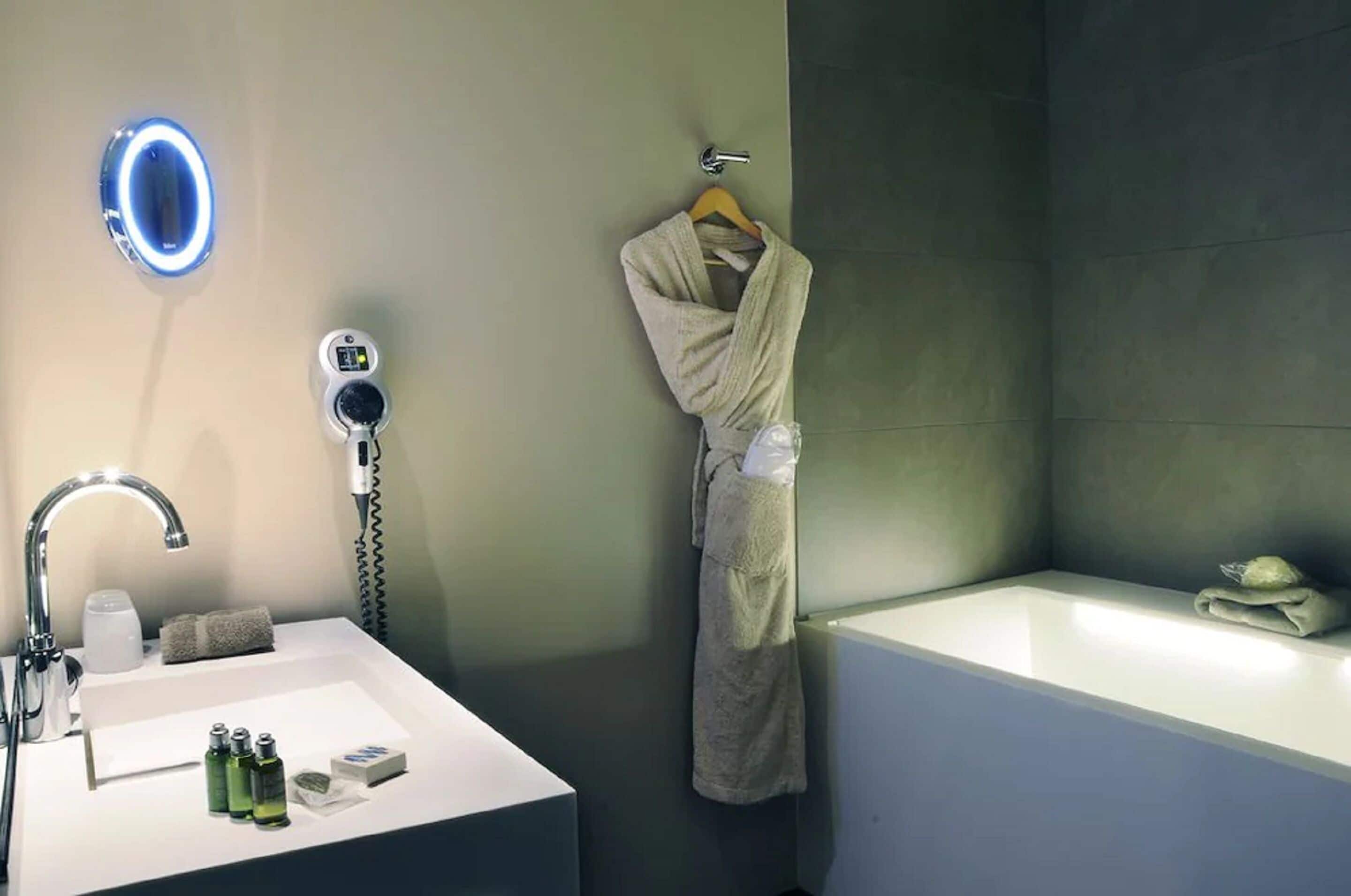 A modern bathroom with a white sink, a handheld showerhead, a robe hanging on a towel rack, and a bathtub.