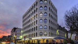 A modern building with a unique geometric facade, featuring multiple circular windows and a ground-level cafe area with outdoor seating. - Best Western Premier Why Hotel (Lille)