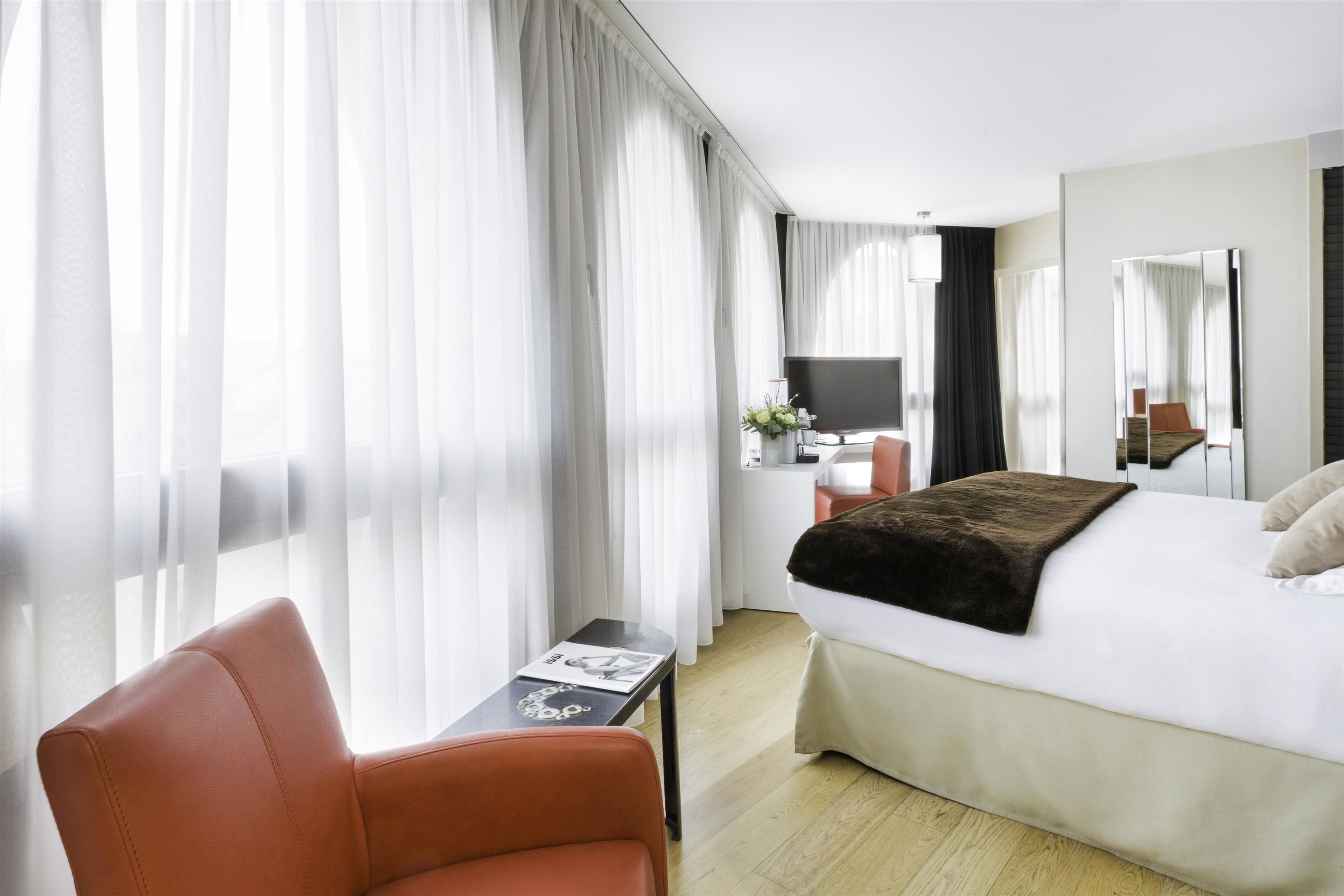 A hotel room with a bed, a desk, a chair, and a large window with curtains.