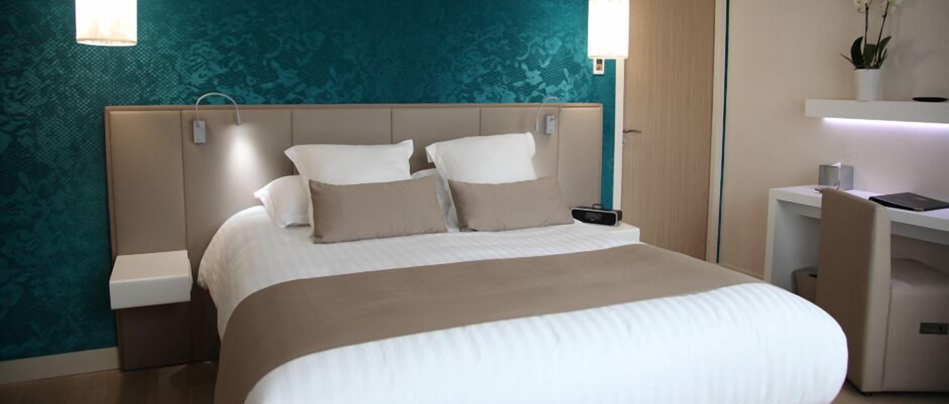 A hotel room with a bed, bedside tables, a desk, and a chair.