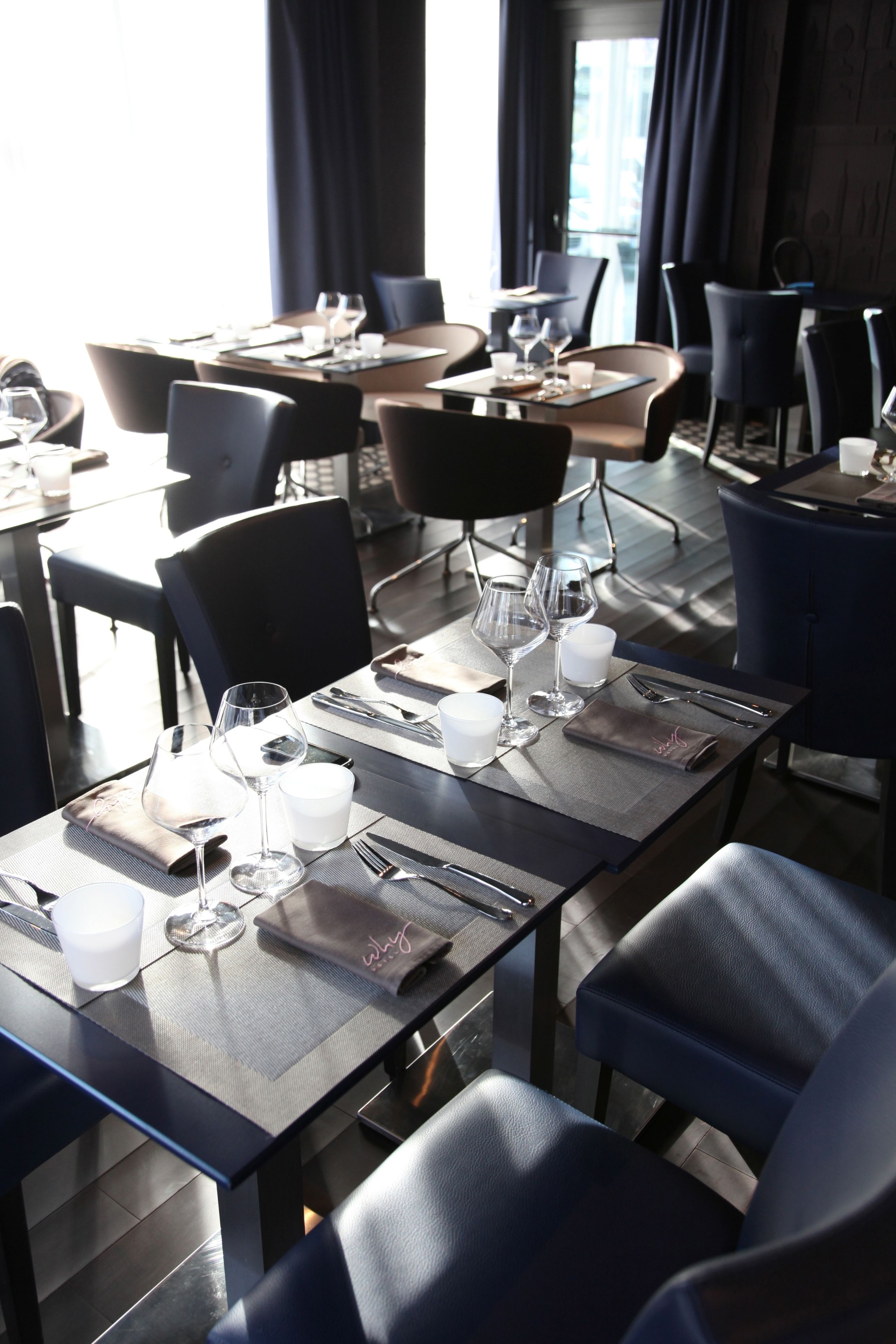A dining area with tables set for two, each with a pair of wine glasses, cutlery, and a napkin.