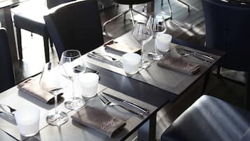 A dining area with tables set for two, each with a pair of wine glasses, cutlery, and a napkin.