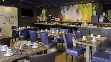 Un restaurant avec des tables dressées pour le service, un bar où l’on sert des boissons et un grand écran diffusant une image floue.
