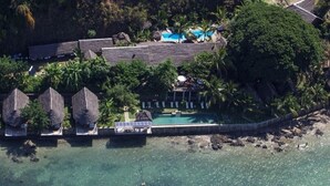 An aerial view of a resort with multiple thatched-roof structures, a swimming pool, and lush greenery. - L'Heure Bleue (Nosy Be)