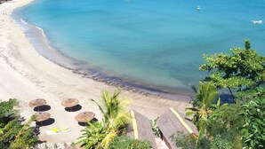 A beach with clear turquoise waters, a sandy shore, and a few umbrellas. - L'Heure Bleue (Nosy Be)
