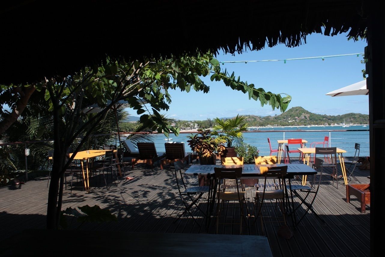 An outdoor seating area with tables and chairs, overlooking a body of water and a distant coastline.