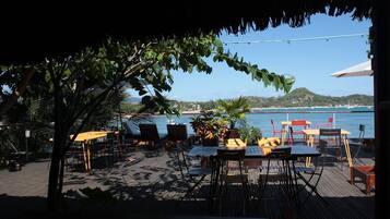 An outdoor seating area with tables and chairs, overlooking a body of water and a distant coastline.