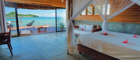 A bedroom with a large bed, a balcony with a view of the sea, and a wooden ceiling.