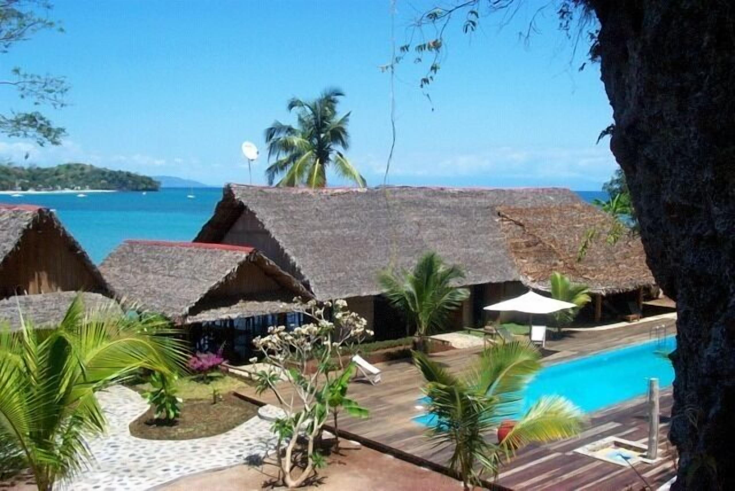 A resort with thatched-roof huts, a swimming pool, and tropical landscaping.