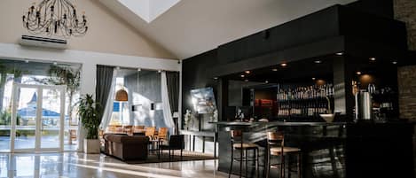 A modern bar area with a high ceiling, a chandelier, and a seating area with a sofa and chairs.