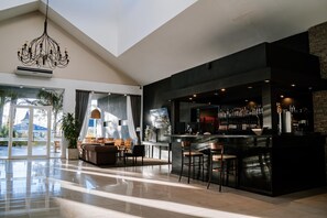 A modern bar area with a high ceiling, a chandelier, and a seating area with a sofa and chairs. - Howard Johnson Hotel & Convention Center Madariaga Carilo (Carilo)