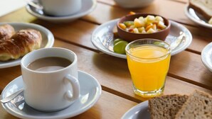 Una colazione con caffè, succo d'arancia, croissant e una ciotola di frutta su un tavolo di legno.