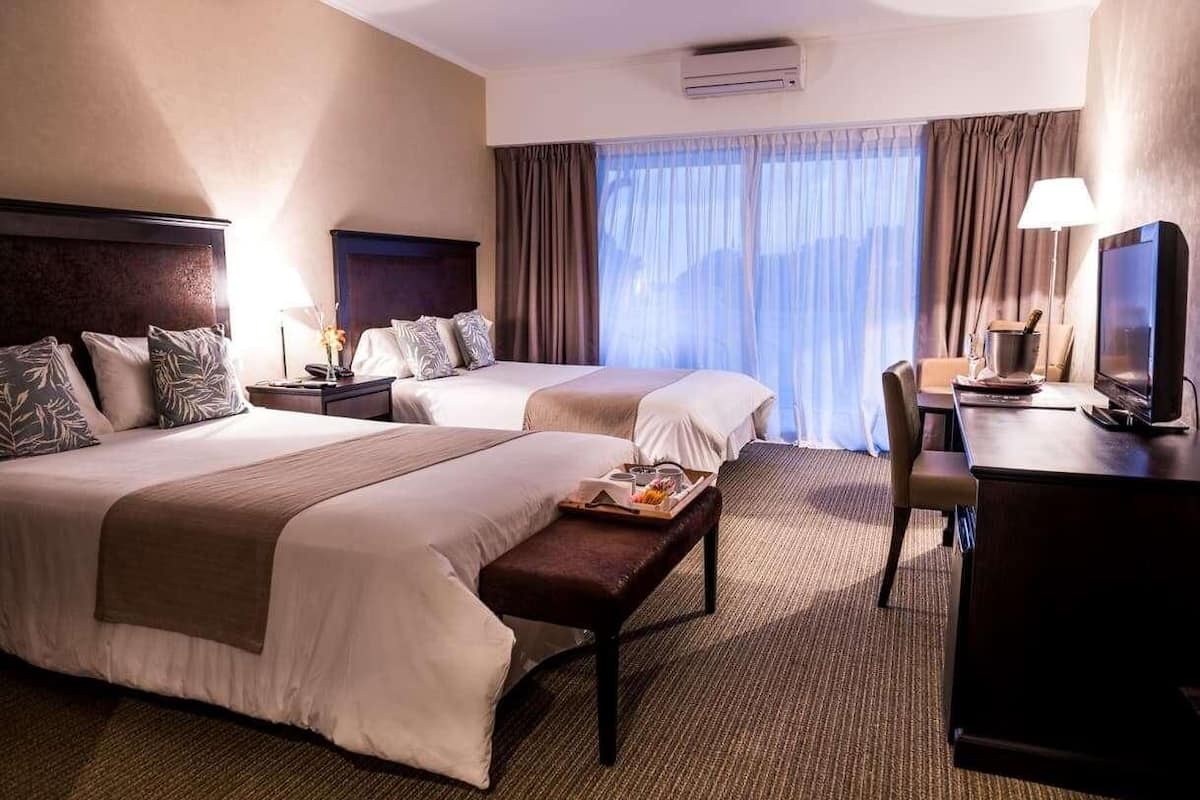 A hotel room with two beds, a desk, a TV, and a window with curtains.