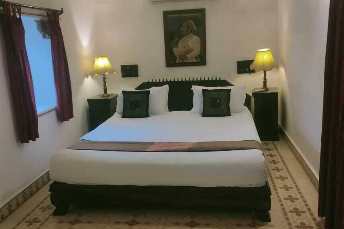 A bedroom with a bed, two bedside lamps, a ceiling fan, an air conditioning unit, and a patterned carpet.