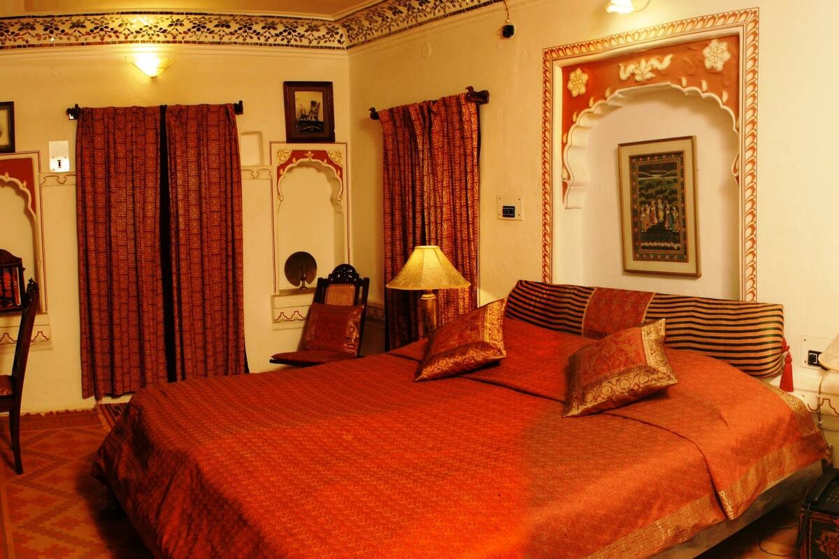 A traditional room with a large bed, a chair, a lamp, and decorative elements.
