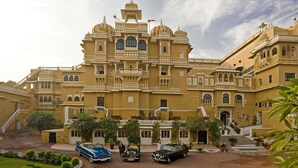 A large, ornate building with multiple balconies and a central dome, surrounded by a well-maintained garden and parked vintage cars. - Deogarh Mahal (Devgarh)