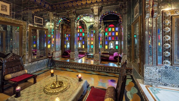 A richly decorated room with ornate furniture, a central seating area, and colorful stained glass windows. - Deogarh Mahal (Devgarh)