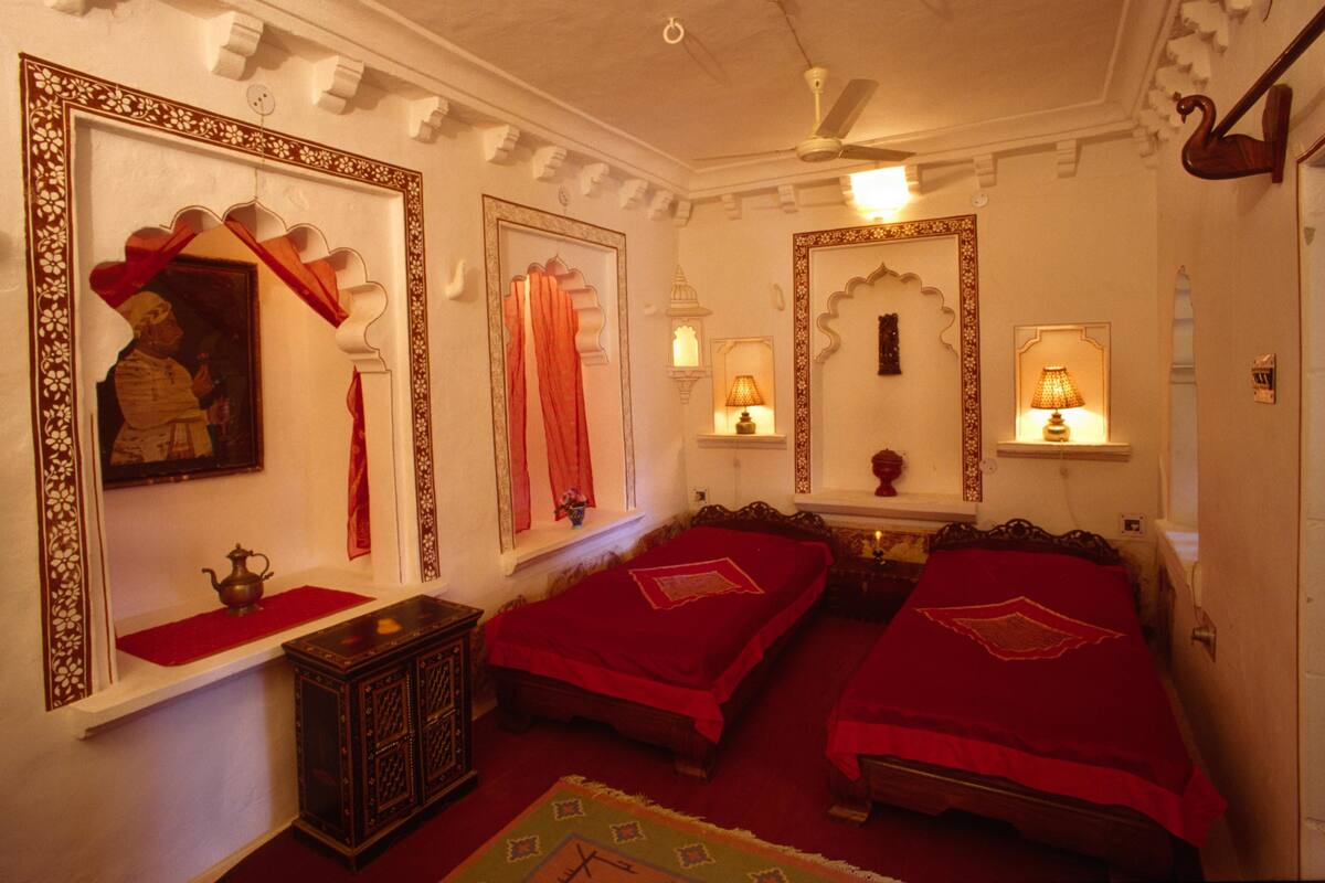 A traditional room with two beds, ornate mirrors, and a ceiling fan.
