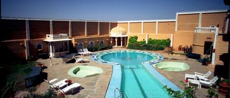 A swimming pool with lounge chairs, a gazebo, and a brick building.