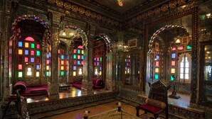 An ornate room with intricate tile work, a central seating area with cushions, and a decorative table with a candle. - Deogarh Mahal (Devgarh)