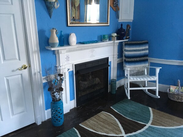 Una habitación con pared azul, repisa blanca de chimenea y una mecedora blanca.