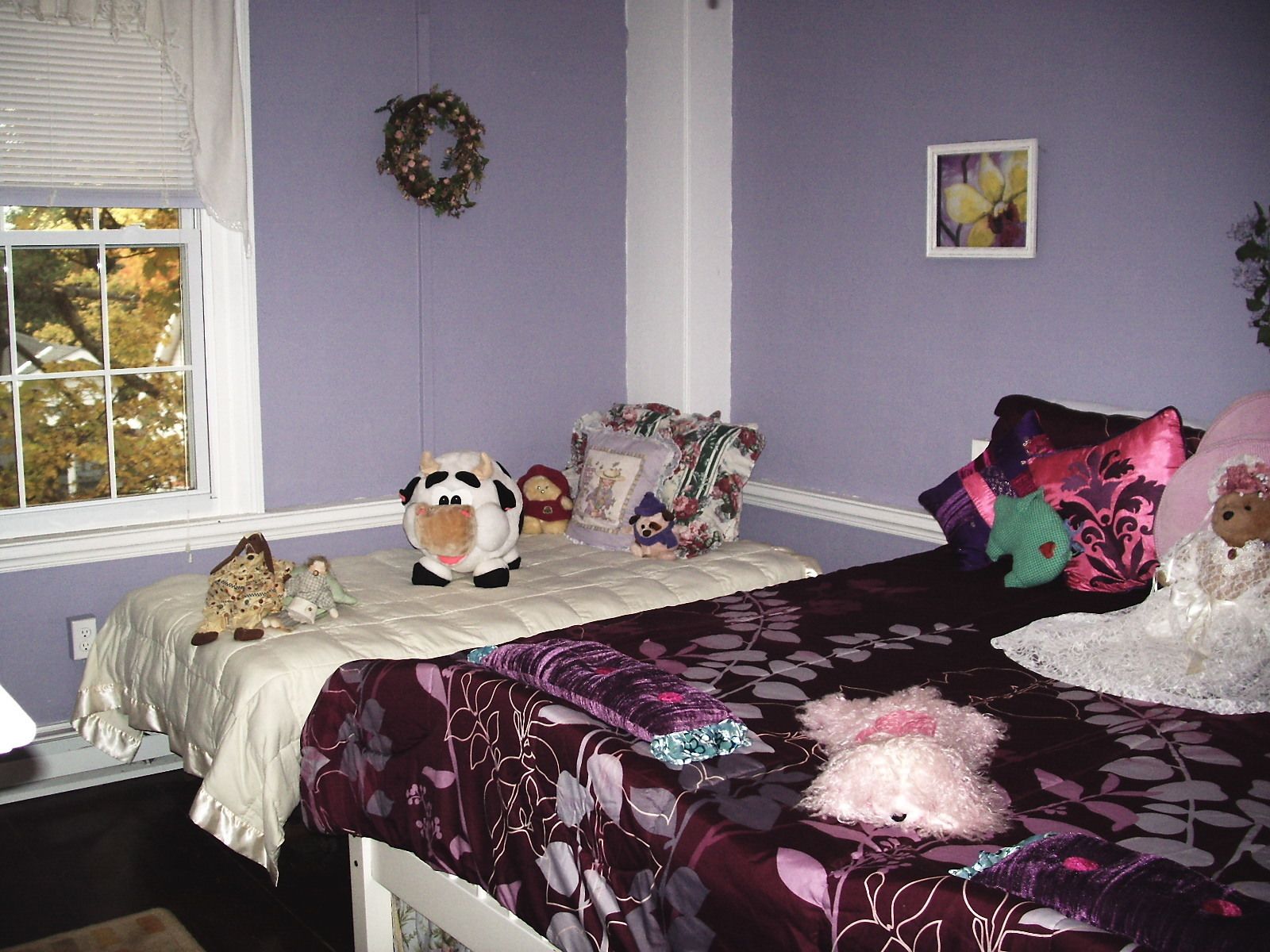 Un dormitorio con cama, ventana, cómoda y una pared decorada con un adorno y un cuadro.
