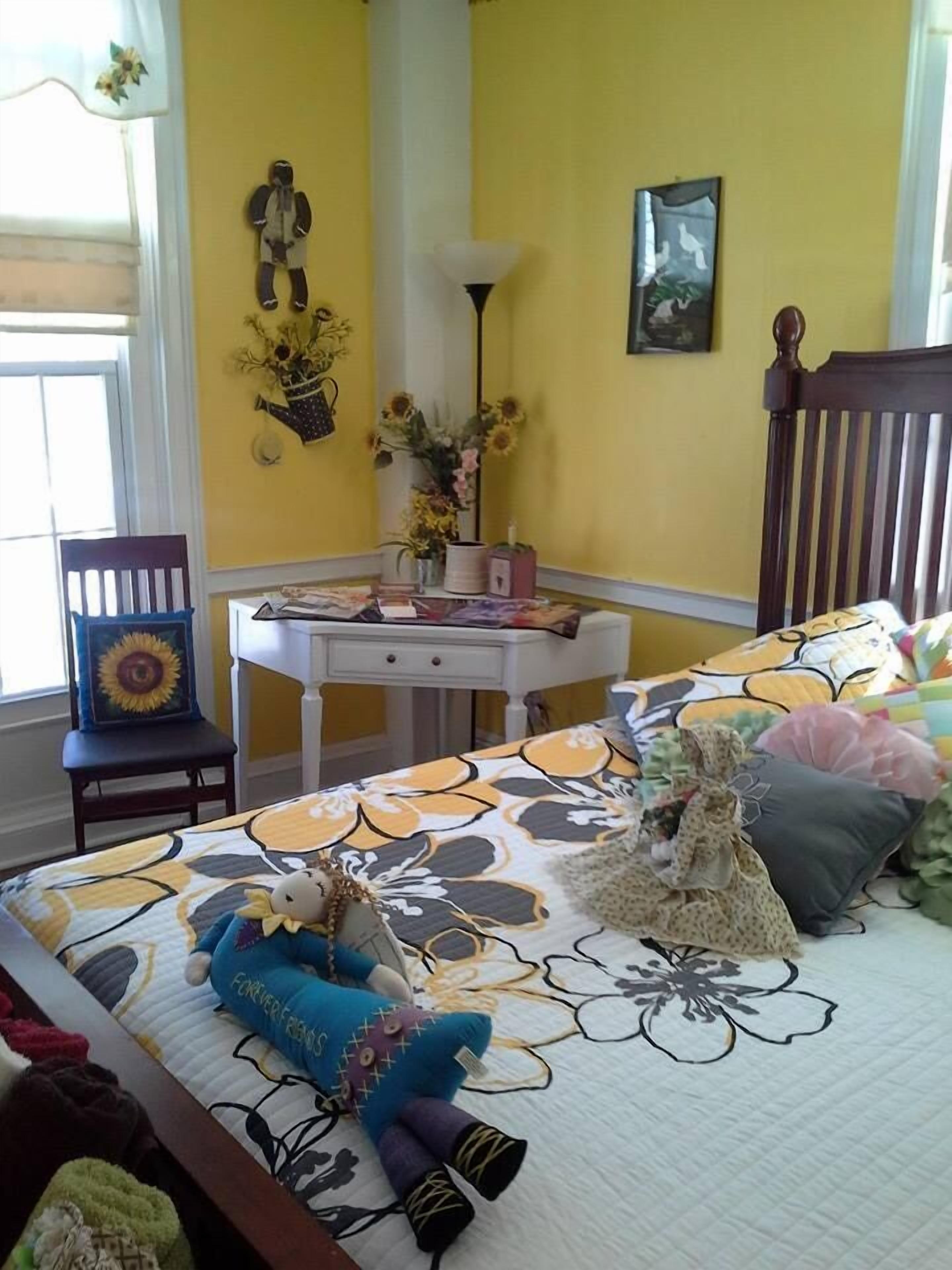 Un dormitorio con una cama, una silla, una mesita de noche y una pared decorada con un cuadro.