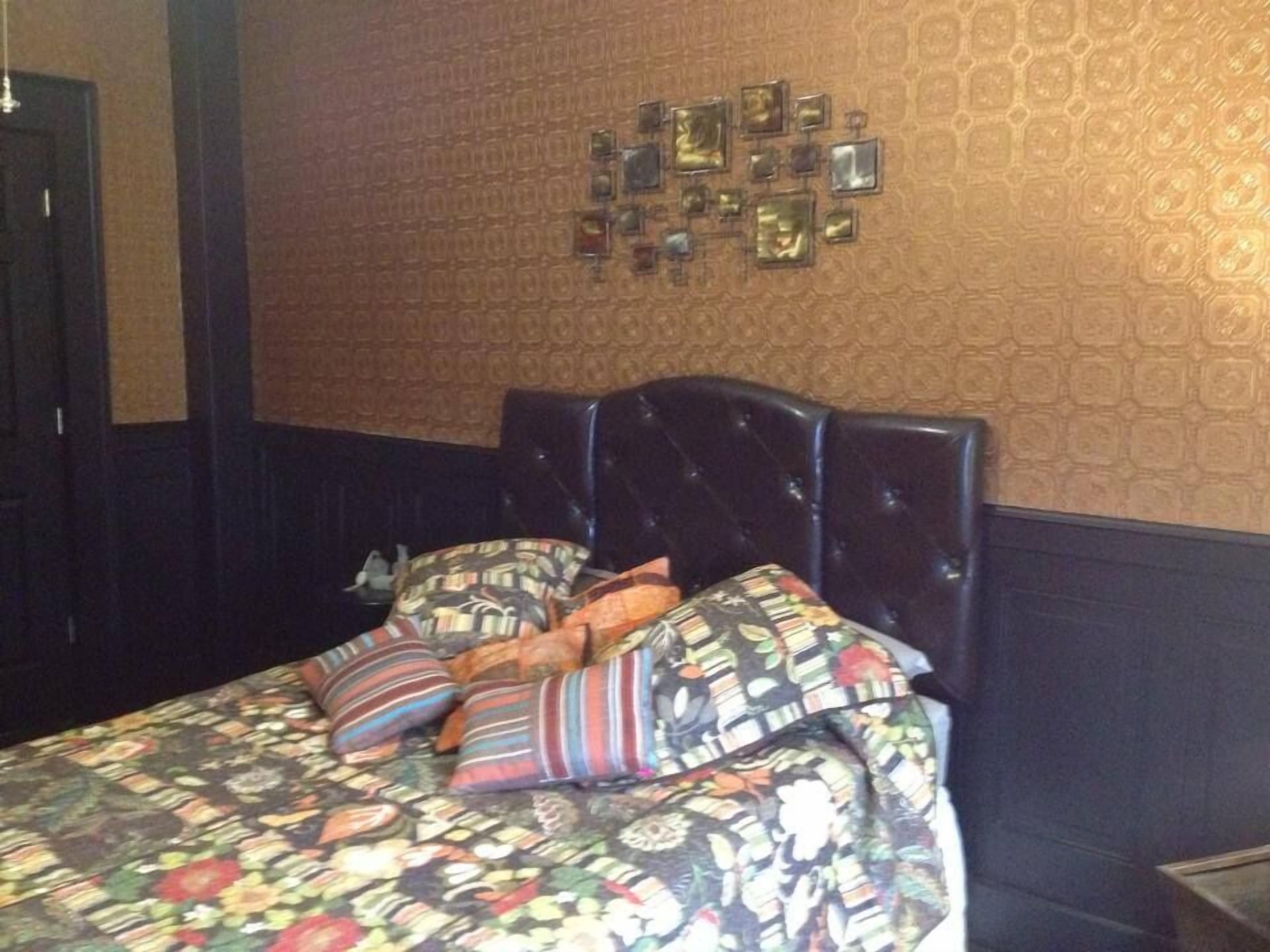 Une chambre d’h ôtel avec un lit, une tête de lit et un mur recouvert d’un papier peint à motifs.